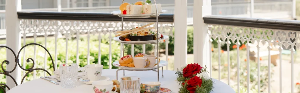 High tea setup with tiered tray, pastries, sandwiches, and tea cups on a veranda.